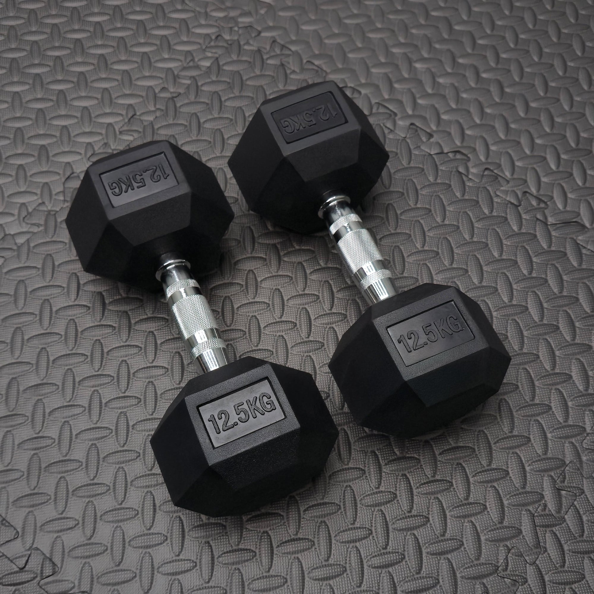 Pair of black 12.5 kg rubber dumbbells on the gym floor
