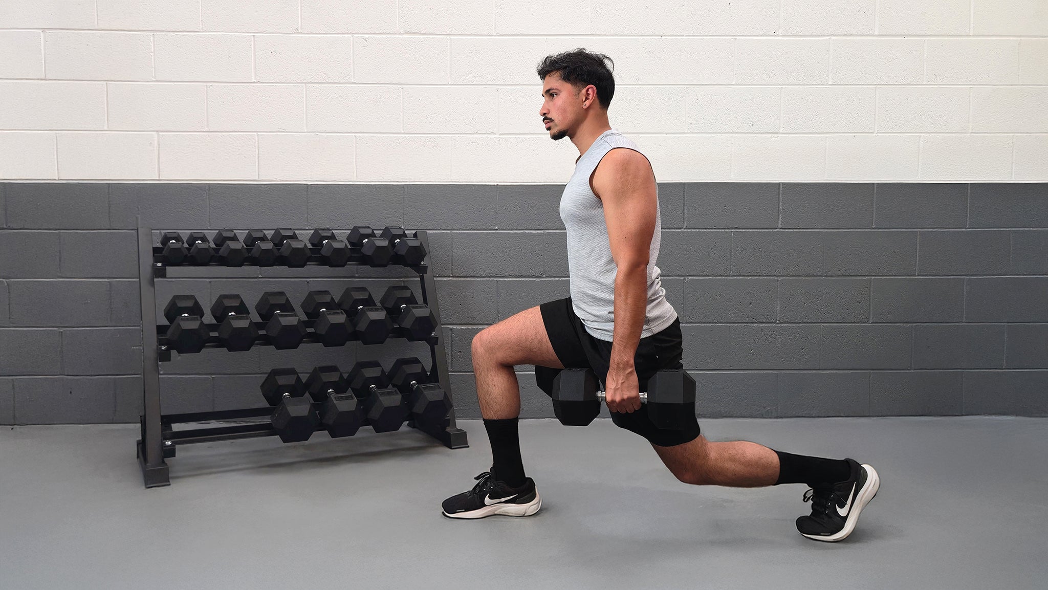 Man performing lunges with dumbbells in a gym setting