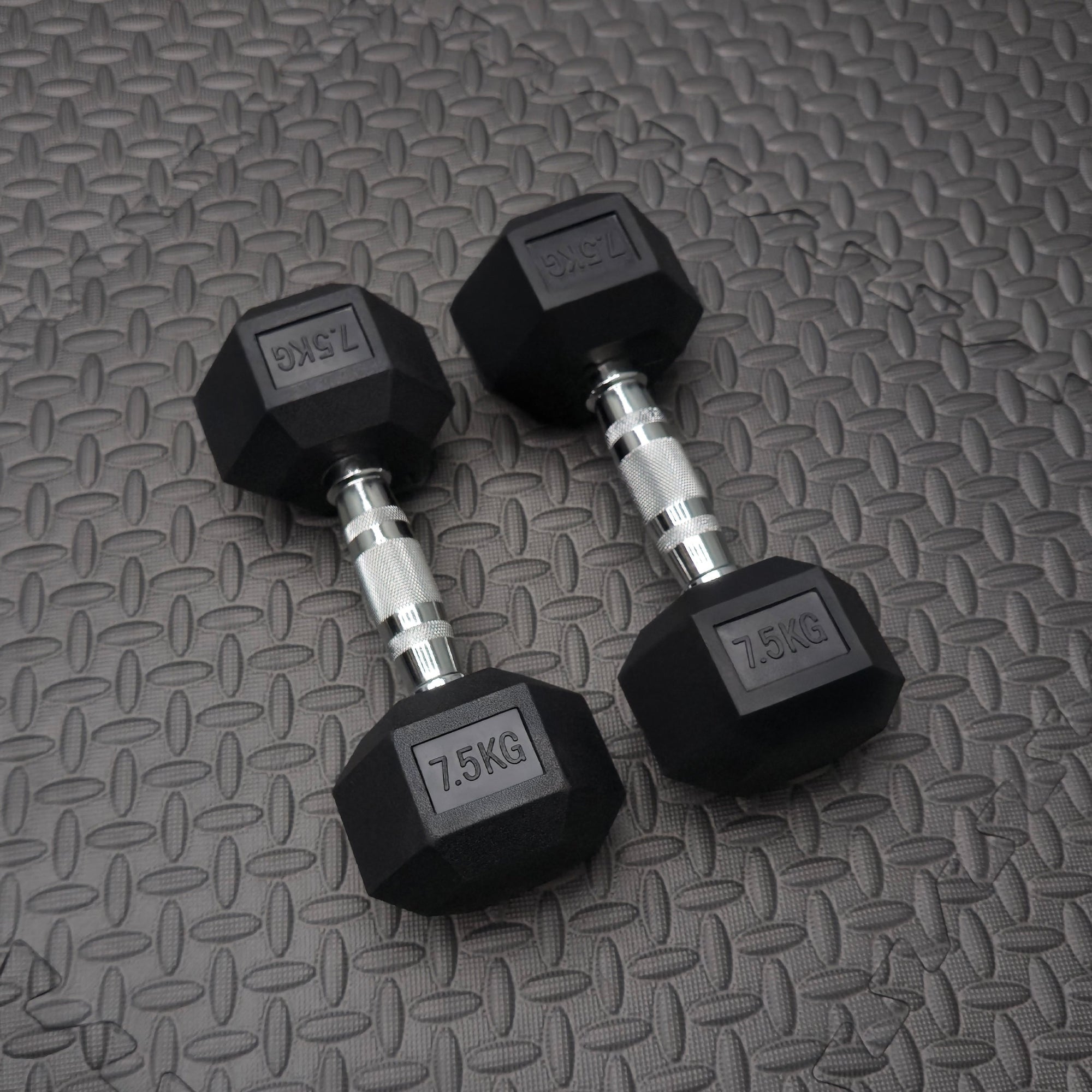 Pair of black rubber dumbbells with '7.5KG' marking on a textured gray surface