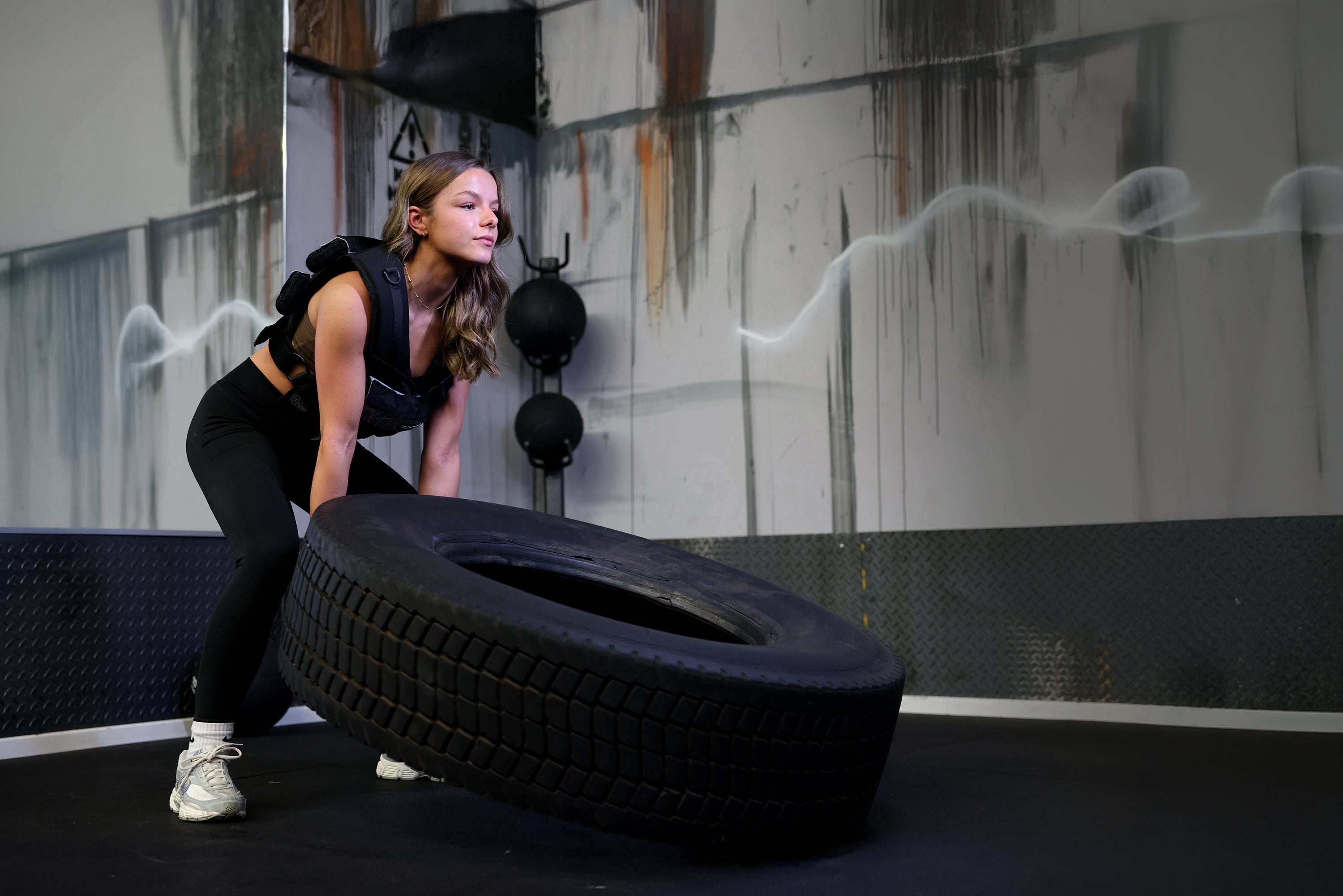 Person lifting a large tire in a gym setting with weight vest on